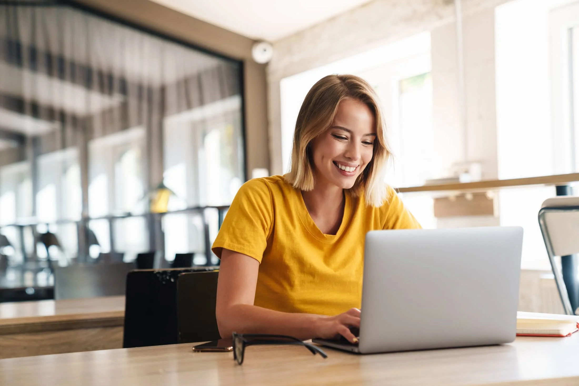 Personal growth coach working on a laptop, smiling while engaging in online coaching or personal development tasks in a bright and modern workspace.